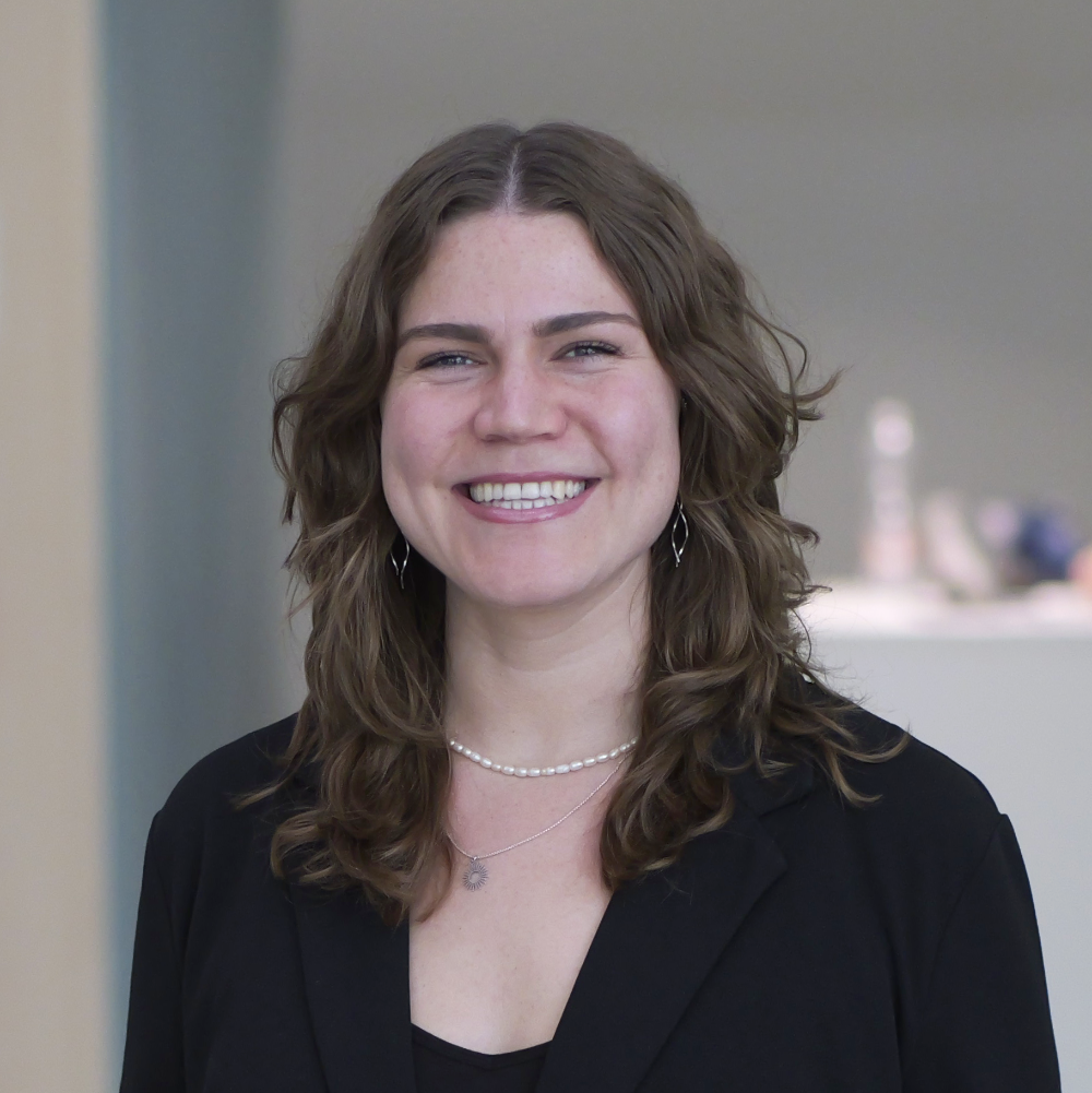 Portrait of a smiling woman with wavy brown hair, wearing a black blazer and a pearl necklace.