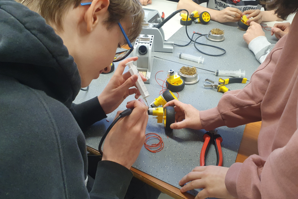 Junge Menschen arbeiten an kleinen Elektro- oder Robotikprojekten mit Werkzeugen und Bauteilen.