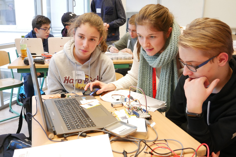 Jugendliche arbeiten konzentriert an einem Laptop mit Elektronikbauteilen im Klassenzimmer.