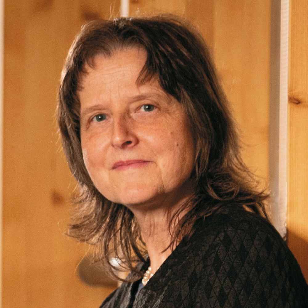 Portraitierte Frau mit dunkelhaarigem Bob, im Hintergrund Holzpaneel.